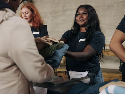 A person handing clothes to a person across a table at a charity.
