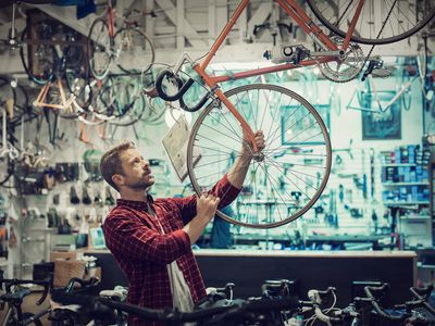 A bike shop owner shifts the front wheel of a display bicycle that is suspended from the ceiling of a narrow store overflowing with new bicycles.