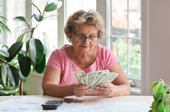 Senior woman sitting at home counting paper money and some pennies