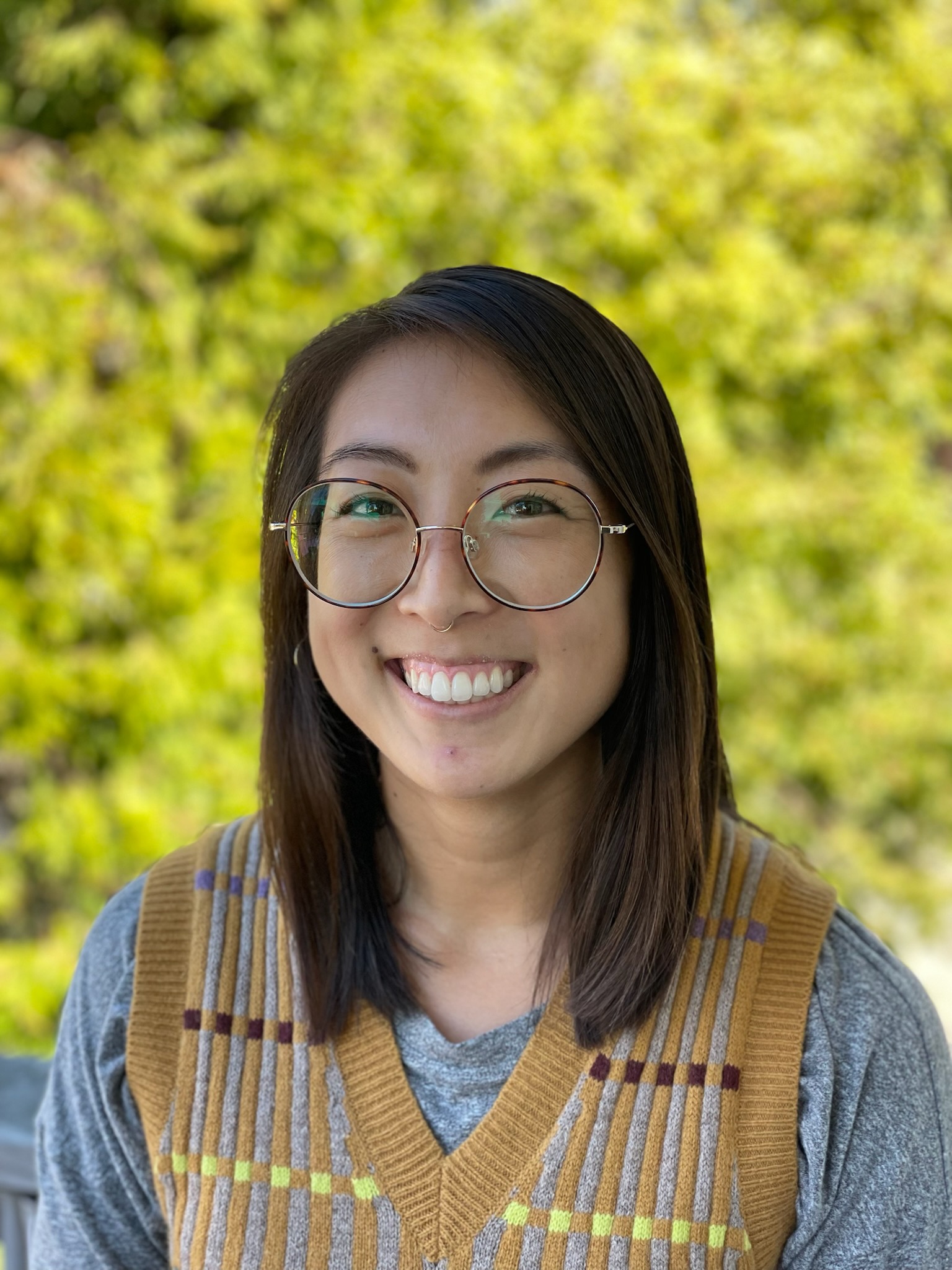 Amanda Young's headshot. Amanda smiles in front of a brick wall wearing a gray long sleeved shirt. Amanda's hair is long, brown, and partly pulled back.