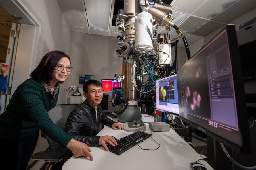A woman, left, and a man look at visual data on several monitors with components of an electron microscope nearby.