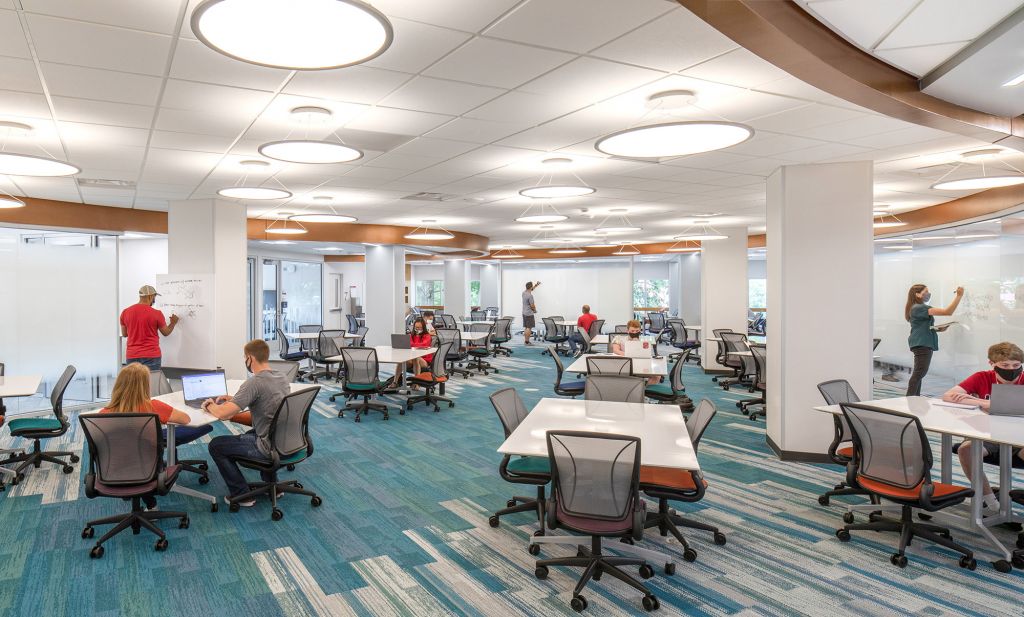 Large, well lit room with lots of tables and chairs. Students in masks are studying and drawing diagrams on whiteboards