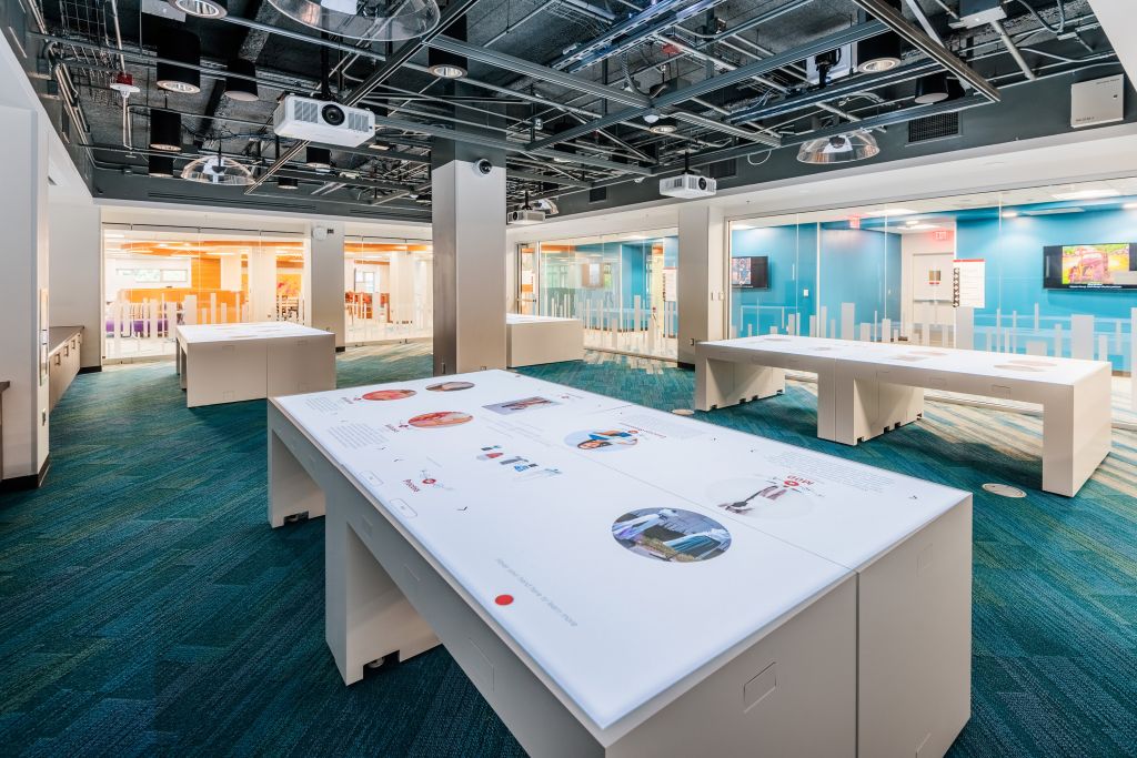 The Innovation Studio's gallery tables display interactive exhibits; above is a grid system hosting projectors, lights, and sensors.