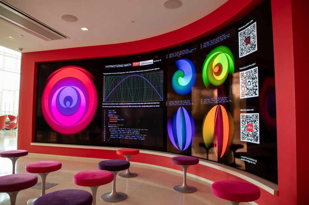 Stools in front of the large, curved screen of the Immersion Theater. The screen shows visuals from an exhibit called 