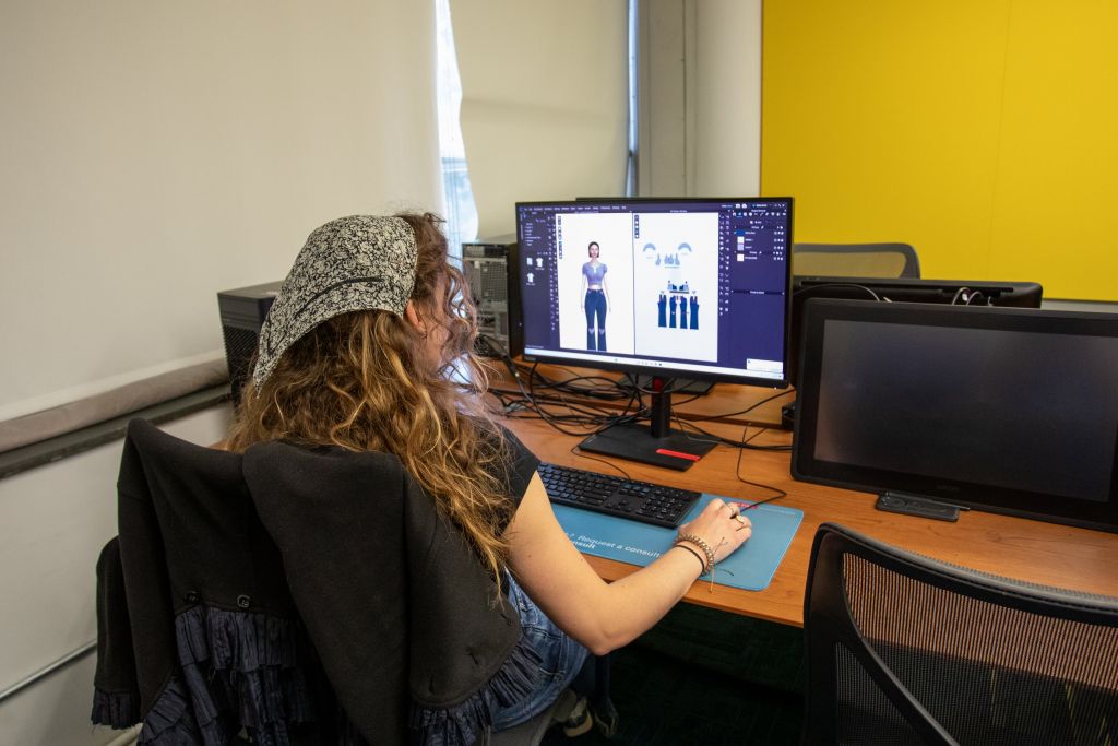 The artist is working on a dual-monitor setup. The screen shows a digital illustration of a character with various poses and elements, indicating work on character design or animation.