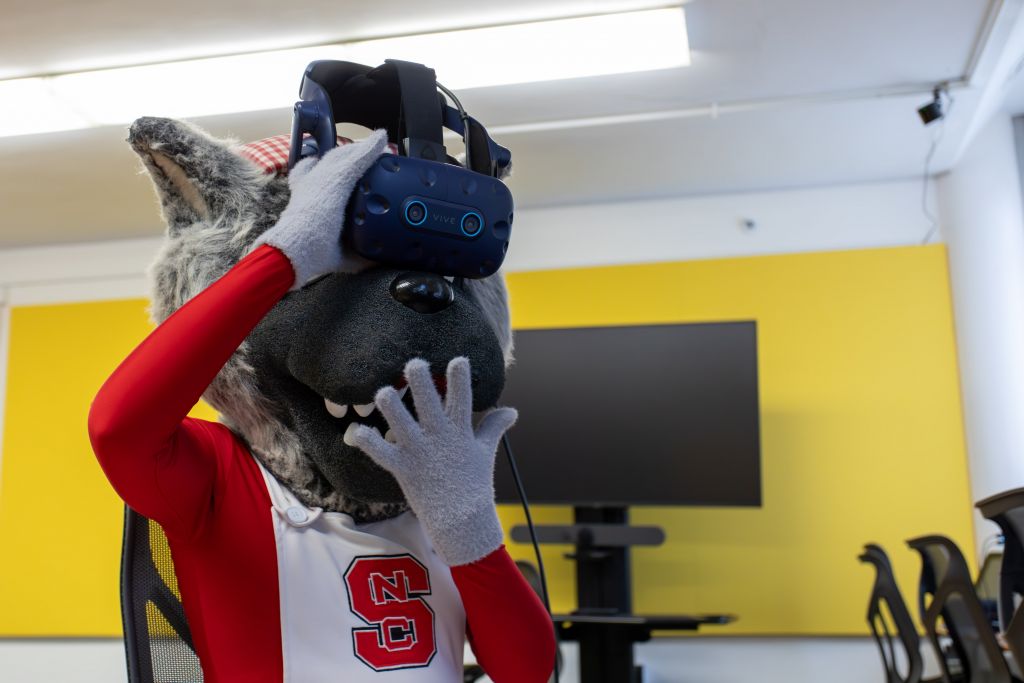 Ms Wuf wears a VR headset and is surprised with the virtual environment. The mascot's expression suggests excitement and engagement.