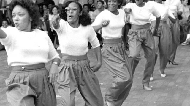 A line of Black women do a step performance in front of an audience