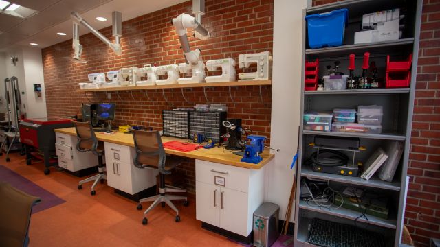 Work tables with a row of sewing machines and shelves containing button makers and crafting supplies