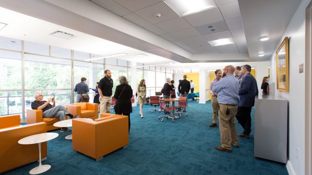 Many faculty members chatting in a bright room with modern, colorful furniture