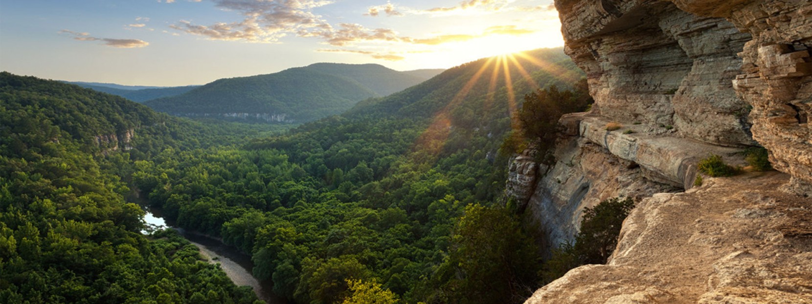 The sun sets over an expansive view of the Ponca Wilderness from a narrow bluff ledge.