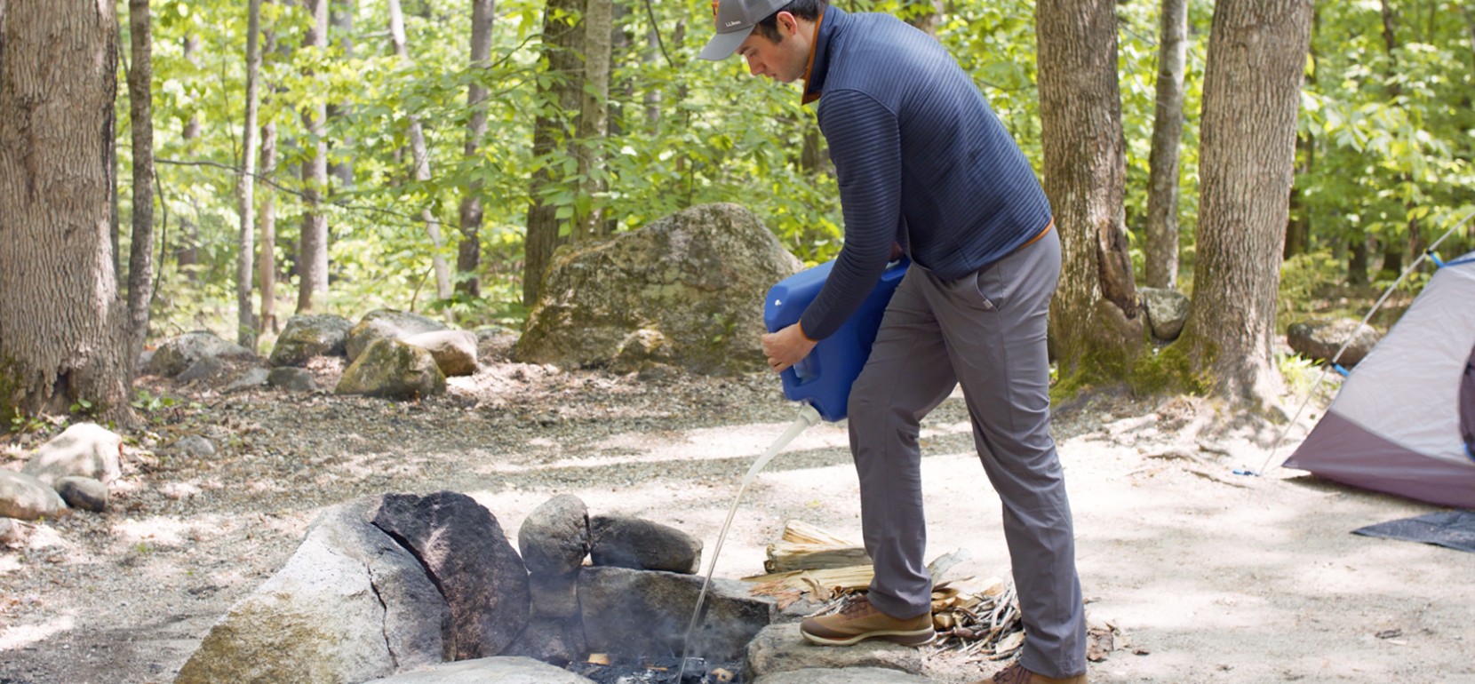 Nate pouring water onto the remains of a fire in a fire ring.