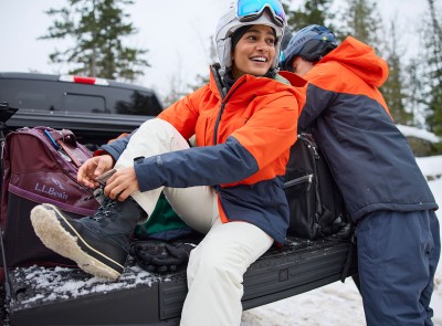 A couple getting ready to alpine ski at the tailgate of a truck.