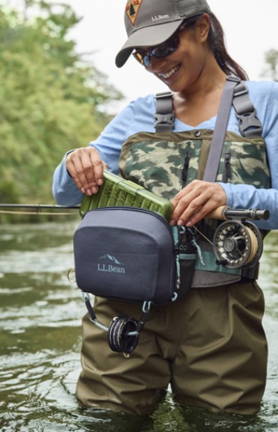 Woman fly fishing on a river, reaching into her fishing pack