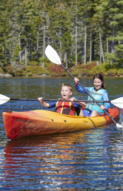 Two children are kayaking on a serene lake, surrounded by trees, enjoying a peaceful outdoor adventure. 