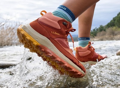 A close-up of hiking footwear on a person walking across a shallow stream.