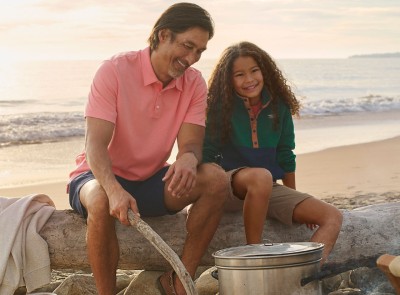 Father and daughter sitting on a log on the beach by a campfire.