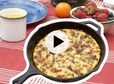 A frittata in a cast iron skillet sits on a picnic table.