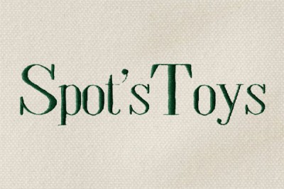 The words "Spot's Toys" monogrammed in green thread in Times Bold on cream-colored canvas.