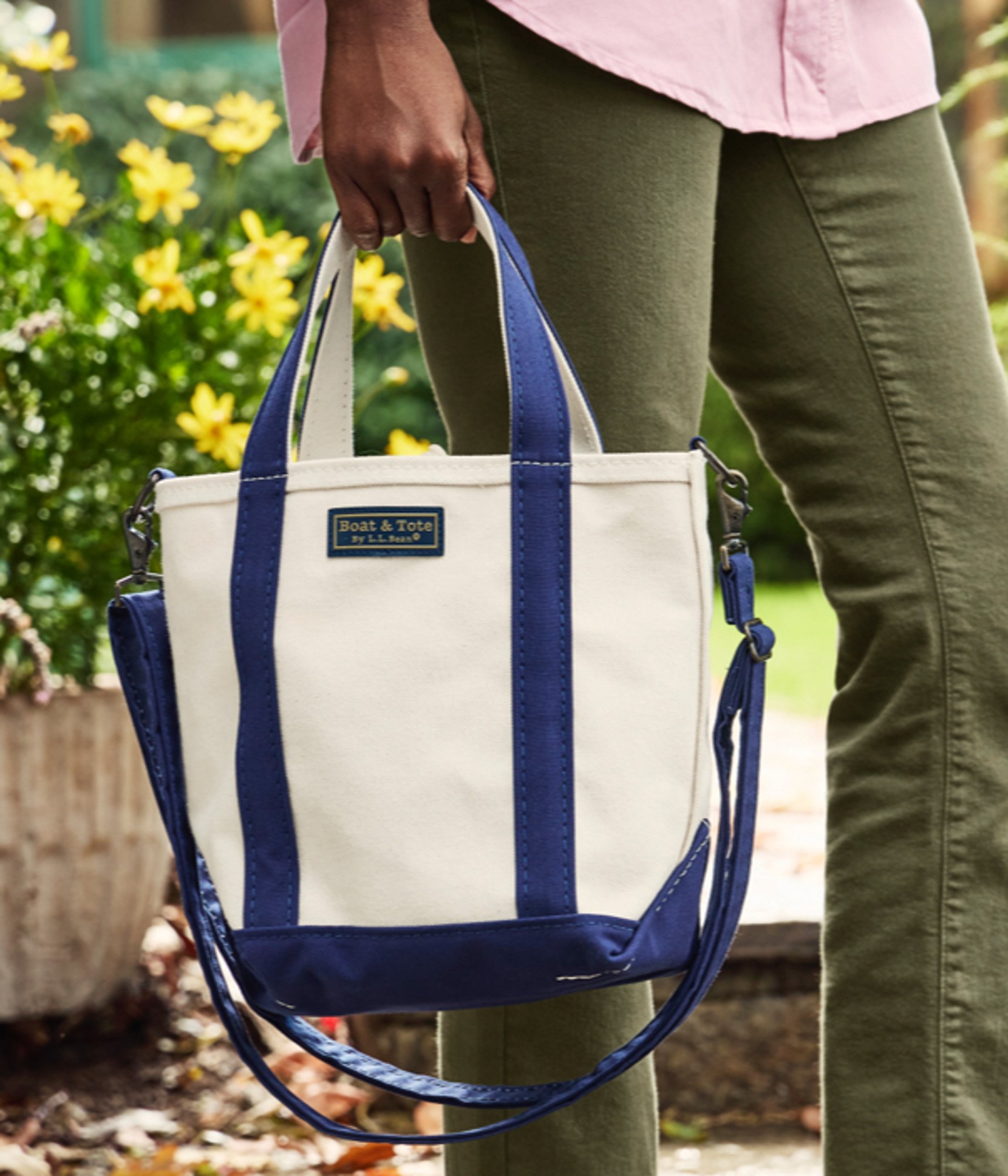 A person outdoors holding a white tote with blue trim.