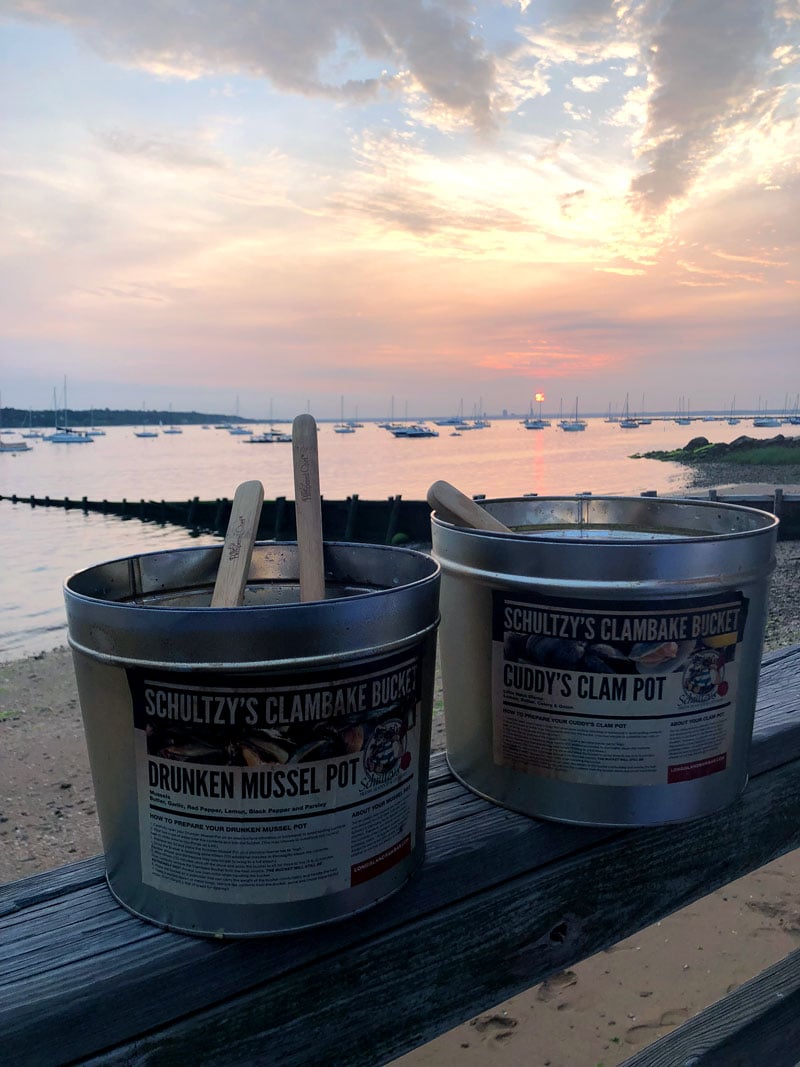 two-schultzys-clambake-buckets-sitting-on-a-ledge-in-front-of-a-beautiful-sunset