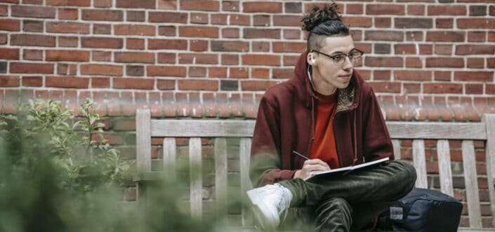 Hombre escribiendo en un cuaderno mientras está sentado en un banco