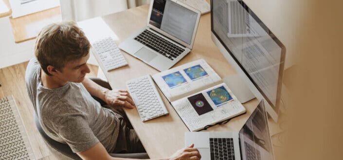 hombre usando 3 computadoras en su trabajo