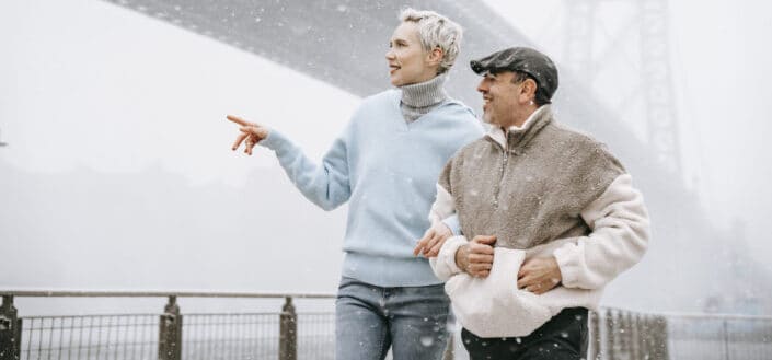 Una mujer más alta caminando del brazo con un hombre más bajo en una nieve fría