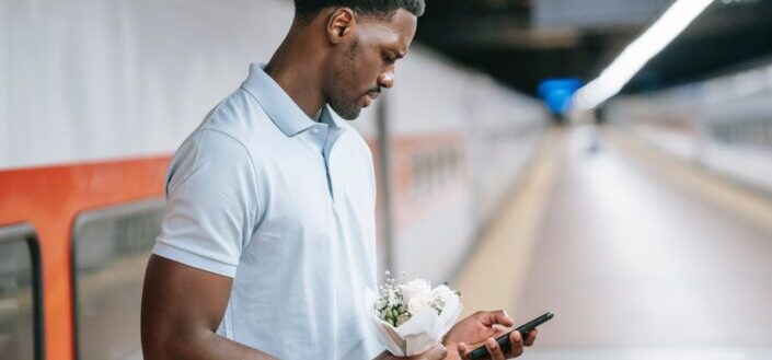 person-in-polo-shirt-holding-cellphone-and-flowers-