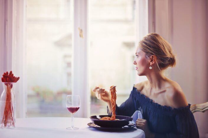 woman-sitting-on-chair-while-eating-pasta-dish-