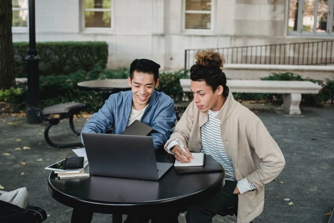 two people sitting outdoor looking at laptop - Productive Things To Do Online