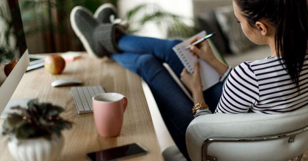 Relaxed woman with her feet up on a desk making a list in a notebook