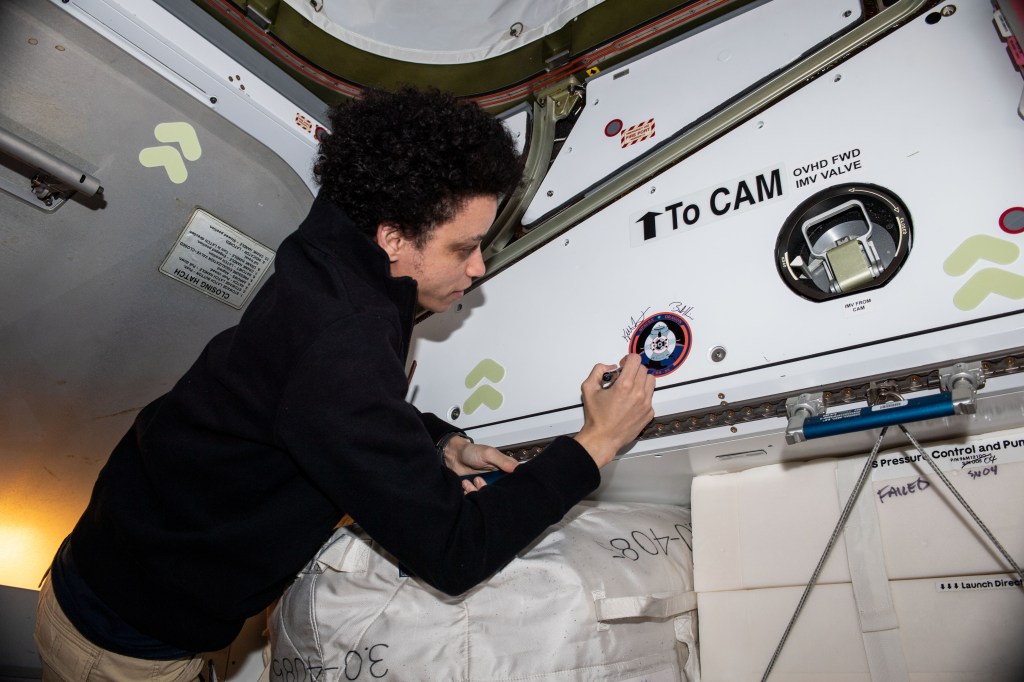 iss068e012458 (Oct. 5, 2022) --- NASA astronaut and Expedition 68 Flight Engineer Jessica Watkins signs her name around the SpaceX CRS-25 mission insignia sticker affixed to the Harmony module's vestibule. Watkins was aboard the International Space Station when the SpaceX Dragon resupply ship docked to Harmony's forward port on July 16, 2022, for a five-week cargo mission.