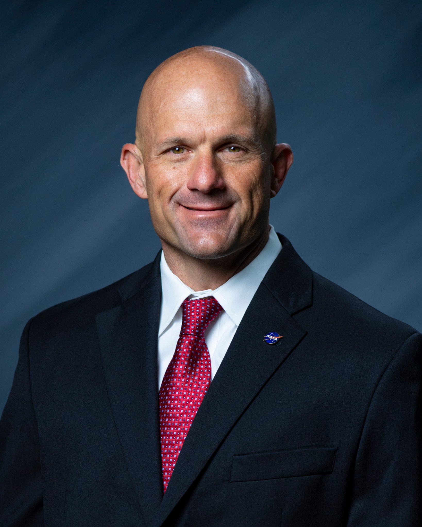 Eli Ouder poses for a NASA portrait wearing a black suit and red tie