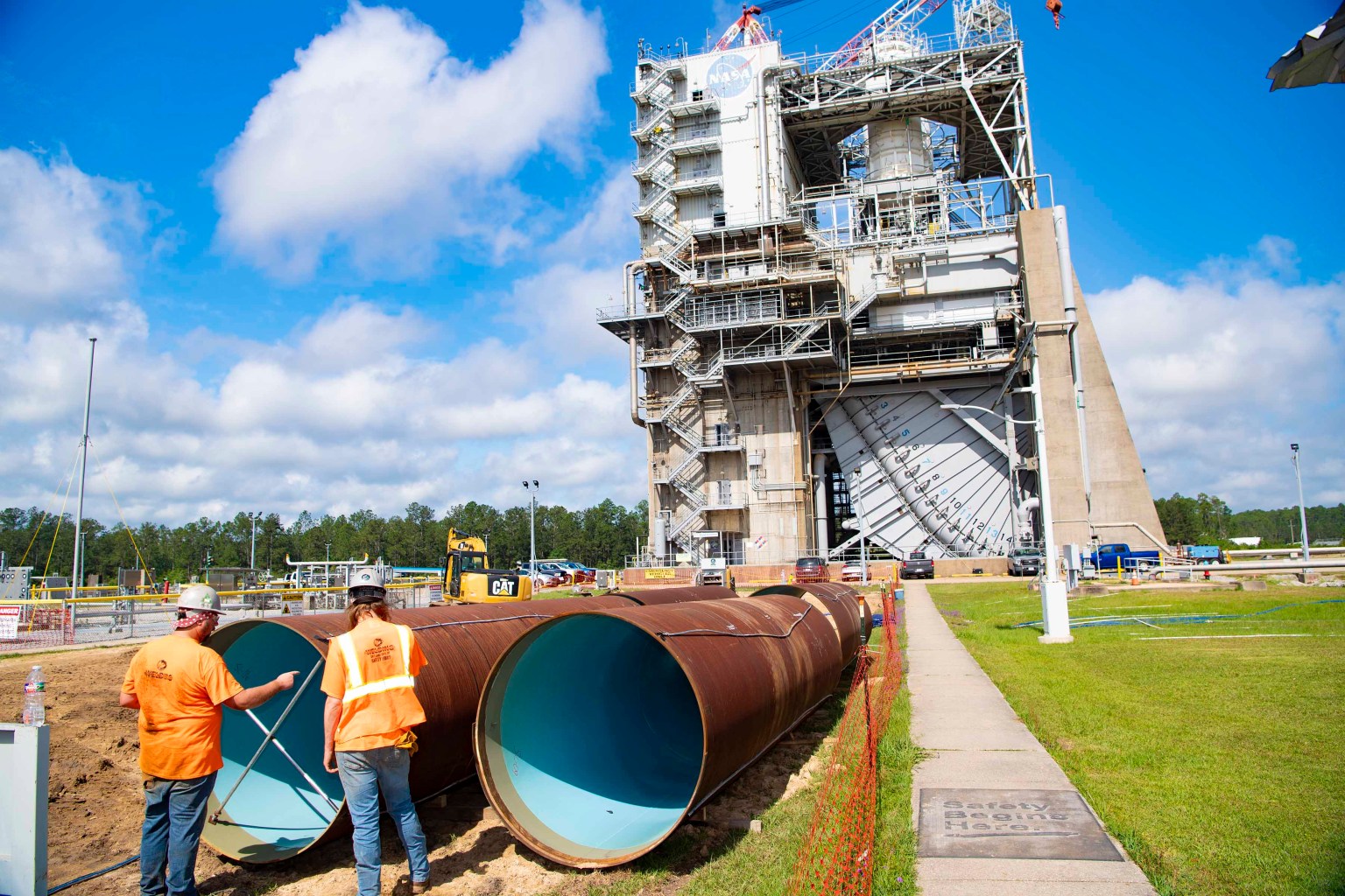 in the cover image of Lagniappe for June 2024, crew members are seen standing near new pipeline sections. the Fred Haise Test Stand is seen in the background