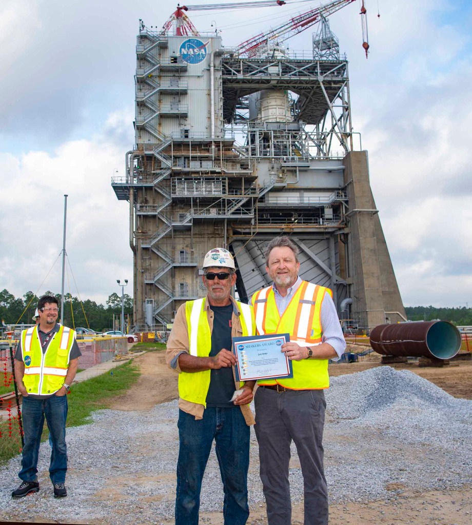 Gary Parker, wearing a white construction hat and yellow safety vest, receives a SHAKERS Award from Rodney McKellip