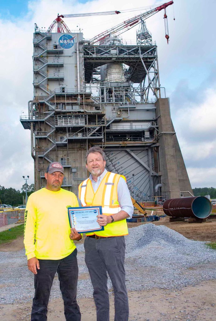 Matt Roberts, wearing a black baseball cap and yellow long sleeve tee shirt, receives a SHAKERS Award from Rodney McKellip