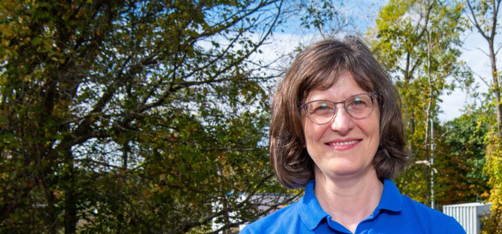 A woman wearing glasses and a blue NASA polo holds up two small cubes, one black and one yellow.