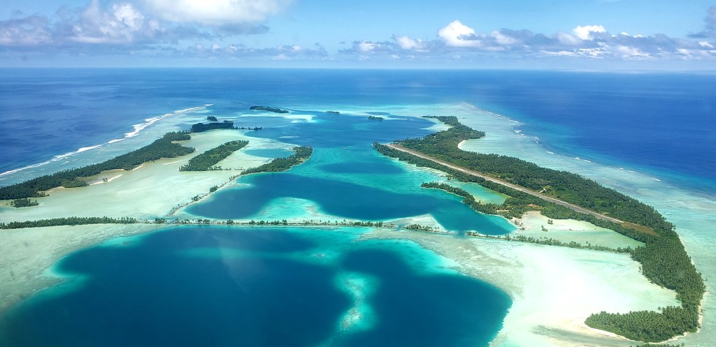 Thin stretches of dark green islands veer together like a capital A. Sandbars rim these islands in a pale blue, which becomes a vibrant teal as the water gets deeper before blending into the deep blue of the ocean.