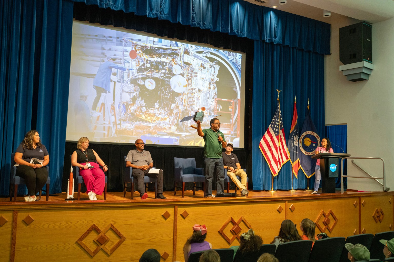 Clyde Conerly, one of the five panelists, shows a satellite replica to the young audience.