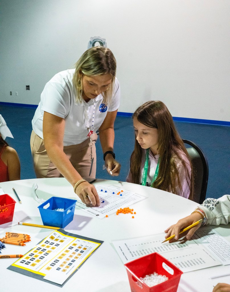 Morgan Necaise, woman in white shirt, assists a Take Our Children to Work Day participant with activity