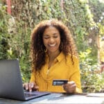 Smiling Brazilian woman using laptop for electronic banking. She is using credit card for online shopping.