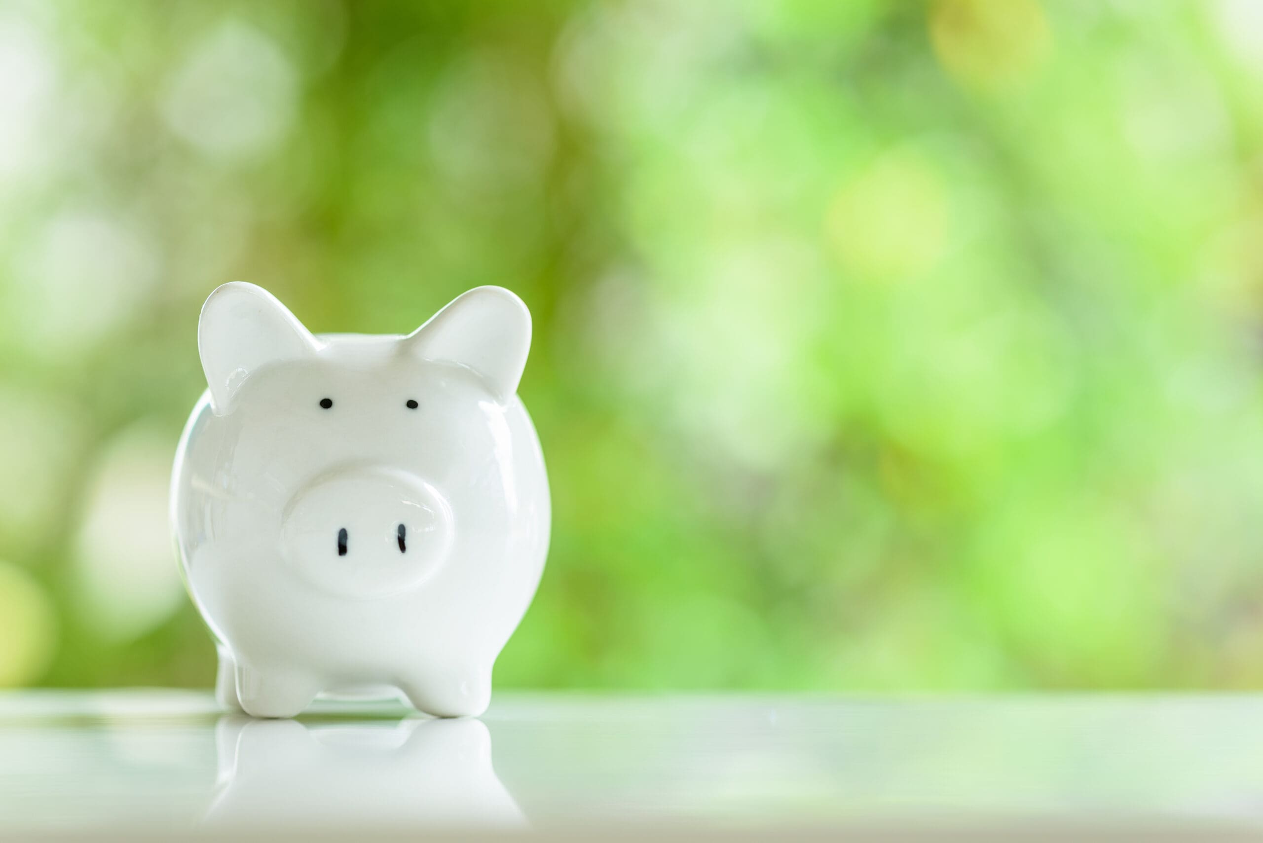 Minor children savings account, financial concept : White ceramic piggy bank on a table with a green bokeh background. The image depicting a type of saving account deposit for child education, allow deposit money from kids for brighter future.