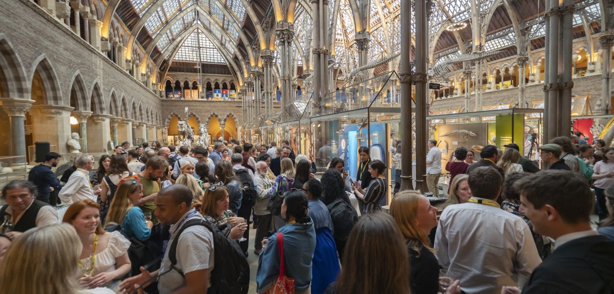 A diverse crowd of different people in the Oxford Natural History Museum – an ornate building with decorative stone pillars and a glass roof.