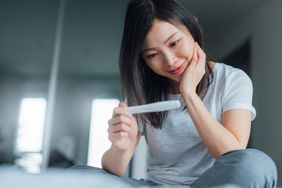 Young woman holding home pregnancy test and looking happy in bedroom