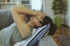 Woman laying on a couch with her hands on her head