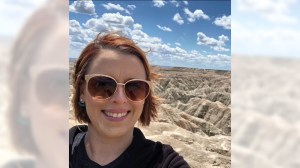 A woman in sunglasses smiles in front of a desert landscape