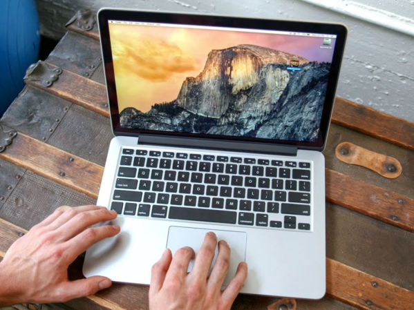 A person using a 2015-era Macbook on a wooden table