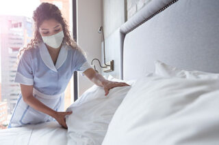 photo - Hotel Maid Making Bed and Wearing Mask