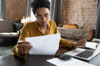 photo - Young Woman Looking at Bill with Calculator and Laptop on Table