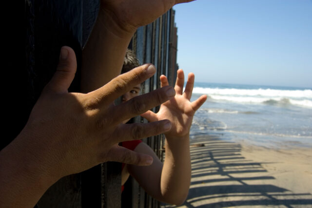 photo - Hands and a Child's Face Poking through Border Fencing